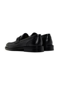 Mocasines de cuero negro con textura suave, punta redondeada y pequeño detalle de herrajes. Suela negra resistente con altura de tacón moderada.