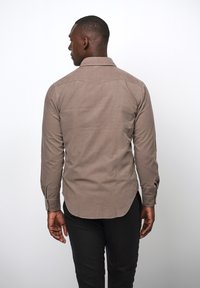 Bruine lange mouwen shirt, lichtgewicht stof, rechte zoom, rugpanelontwerp en knoopmanchetten, gedragen met zwarte broeken.