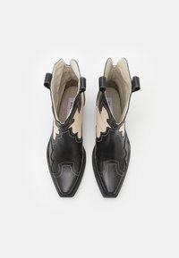 Sorte og beige lær ankelstøvler med spidse tær, bølget design, kontrasterende søm og trækflapper på siderne.