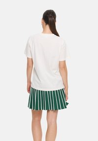 T-shirt blanc à manches courtes associé à une jupe plissée verte avec des rayures blanches, mettant en avant un design de tenue décontractée et superposée.