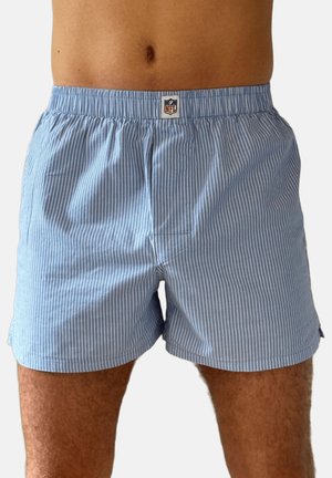 Man wearing light blue and white vertical striped NFL boxer shorts, shown from waist to mid-thigh against a white background.