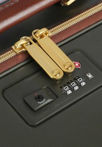 Chiusura con zip dotata di doppi cursori in metallo dorato, corpo nero testurizzato e combinazione con lucchetto a manopola regolabile in un design compatto.