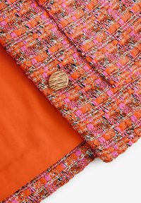 Kollane tweed kangas roosade ja lillade aktsentidega. Omab tekstureeritud pinda ja suurt, ümmargust tekstureeritud nööpi. Sisekate on ühtlane kollane.