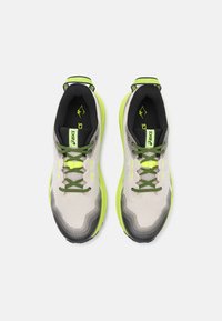 Zapatillas deportivas en gris y blanco con parte superior de malla transpirable, detalles en verde y suela negra texturizada. Presenta cordones verdes y un logo.