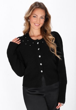 Schwarze Strickjacke mit rundem Ausschnitt, langen Ärmeln und silbernen Knöpfen. Verziert mit kleinen Verstärkungen entlang der Schultern für zusätzliche Details.