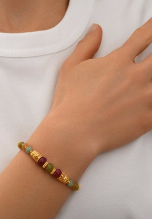 Bracelet coloré en perles avec des accents dorés. Perles vertes, bleues, violettes et brunes, créant une texture et un motif variés.