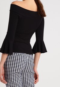 Schwarzes schulterfreies Rippoberteil mit Glockenärmeln, kombiniert mit marineblauen und weißen karierter Hose, die ein figurnahes Design und texturierten Strickstoff zeigt.