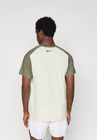 Tricou sportiv cu mânecă scurtă, cu corp de culoare verde deschis și mâneci de culoare verde măslin, având un logo Nike negru pe partea superioară a spatelui.