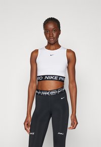 Bijela uska kratka majica s crnim Nike logotipom, uparen s crnim tajicama s brendiranim pojasom i logotipima na nogavicama.