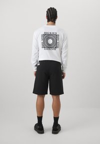 White long-sleeve t-shirt with black geometric graphic on back, paired with black shorts and black sandals. The outfit has a relaxed fit.