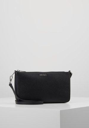 Sort rektangulær crossbody-taske med tekstureret overflade, sølvfarvet "HUGO"-logo, lynlåslukning og aftagelig rem på hvid udstillingspiedestal.
