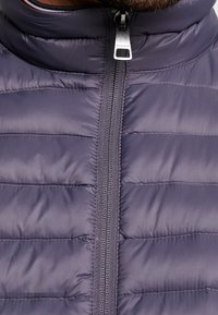 Giubbotto trapuntato blu navy con colletto alto e motivo a cuciture orizzontali. Presenta una chiusura centrale con zip e un tirazip in argento. Texture liscia.