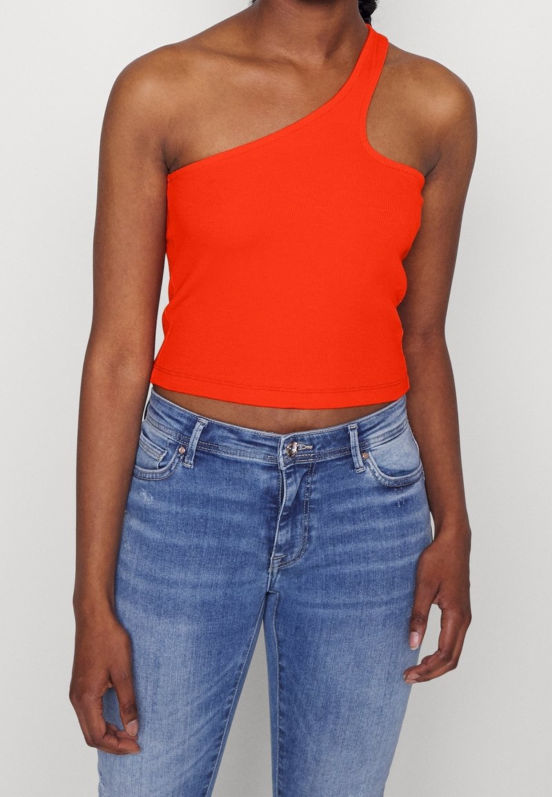 Červený žebrovaný crop top s jedním ramínkem, kombinovaný se světle modrými džíny s fitted střihem a klasickým pěti-kapsovým designem.