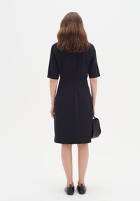 Svart klänning med korta ärmar, figursydd design, knälång, inga synliga mönster, bärs med svarta lägenheter och en liten svart väska.