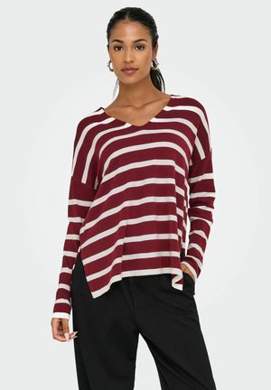 Pull-over V en maroon et blanc rayé à coupe ample et manches longues, avec fentes latérales et tissu doux et texturé. Associé à un pantalon noir.