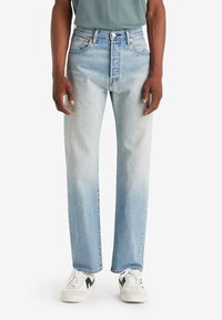 Vaqueros de mezclilla de color azul claro con un diseño de pierna recta, cintura alta y un ligero desvanecimiento. Se llevan con zapatillas blancas con acentos negros.