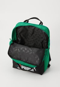 Zaino verde e nero con doppi zip, dotato di un ampio interno e di una fodera nera decorata con il logo Puma.