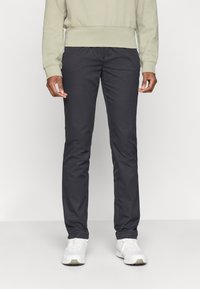 Jūras zilas šauras piegriezuma bikses, izgatavotas no gludas auduma, ar sānu kabatām un maigu spīdumu. Valkātas ar gaiši zaļu sporta kreklu un baltām sporta apaviem.