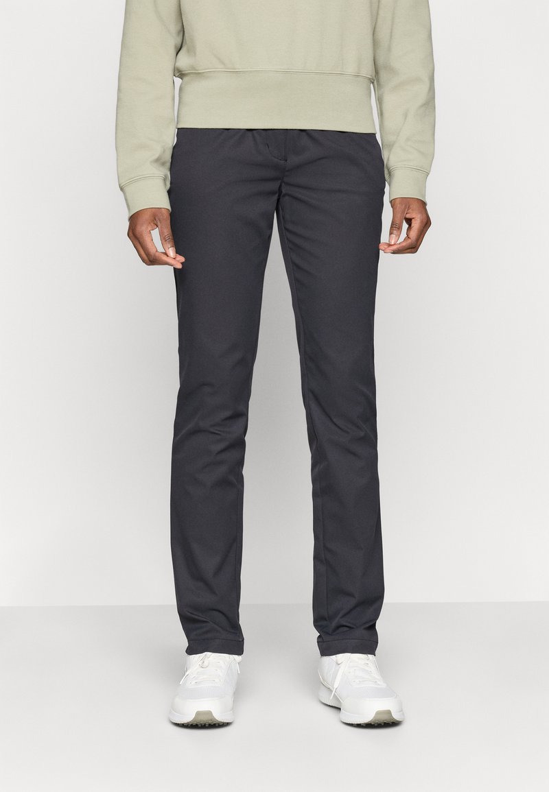 Marineblå smalpassformede bukser laget av glatt stoff, med sidelommer og en subtil glans. Båret med en lysegrønn hettegenser og hvite sneakers.