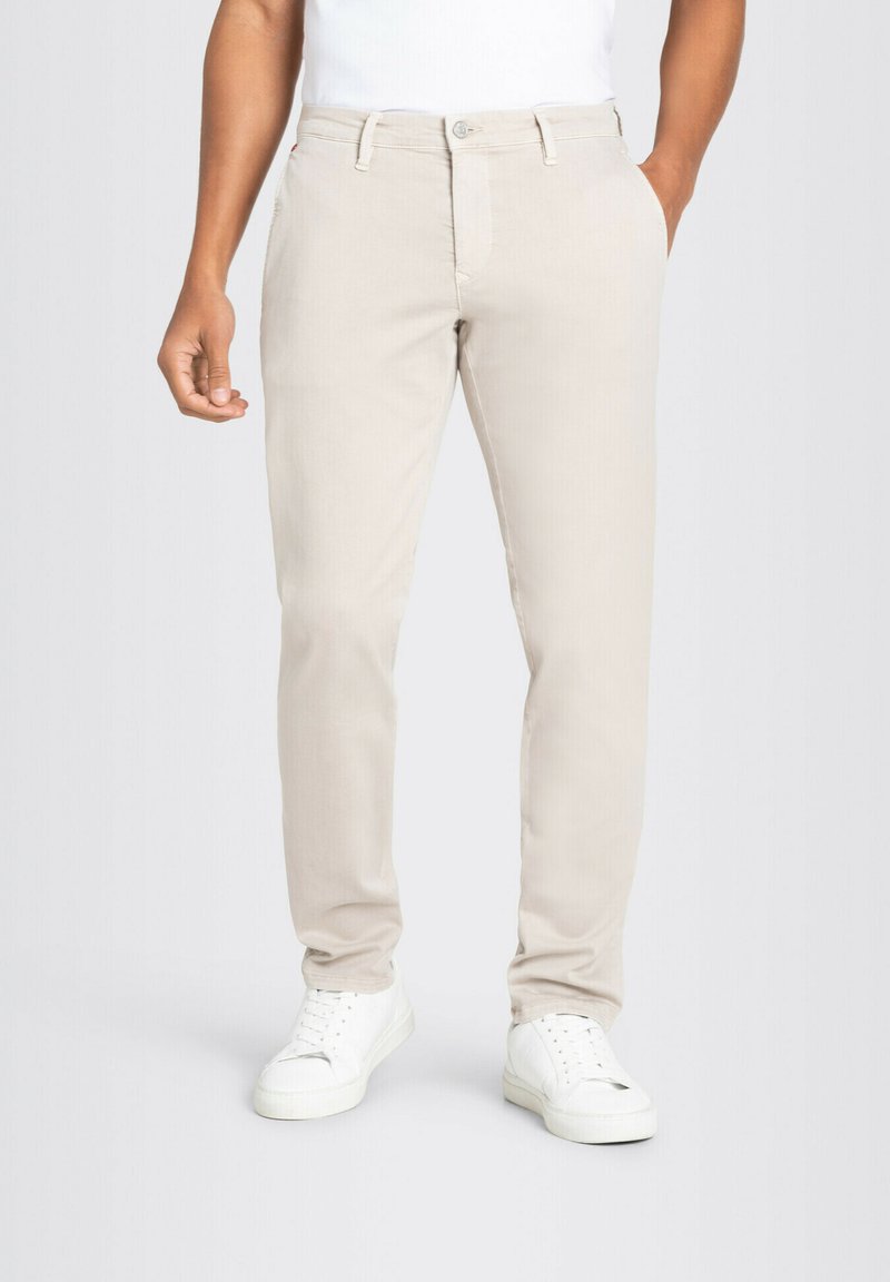 Beige chinos made of cotton, featuring a straight design, side pockets, and a button closure. Worn with white sneakers.
