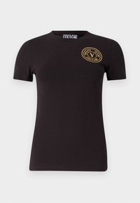 Crna pamučna majica s kratkim rukavima, okruglim izrezom i kružnim zlatnim logom koji sadrži "Versace Jeans Couture" na lijevoj strani grudnog koša.