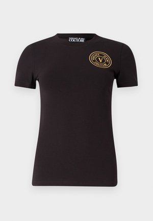 Camiseta de algodón negra de manga corta, con cuello redondo y un logo circular dorado que presenta "Versace Jeans Couture" en el lado izquierdo del pecho.