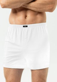 Boxer en coton blanc avec une taille élastique, doté d'une fermeture à un bouton et d'une texture douce, conçu pour le confort.