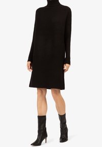 Robe en tricot noir avec une texture côtelée, col montant et manches longues ; associée à des bottines en cuir ajustées noires avec un bout pointu.