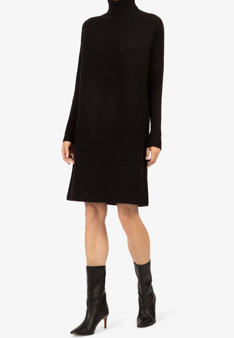 Robe en tricot noir avec une texture côtelée, col montant et manches longues ; associée à des bottines en cuir ajustées noires avec un bout pointu.
