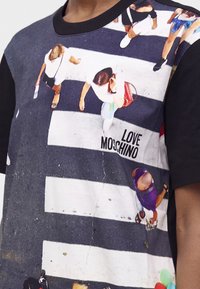 Κοντινή λήψη ενός t-shirt που δείχνει μια εναέρια θέα από ανθρώπους που περπατούν σε διάβαση πεζών με το κείμενο "Love Moschino" πάνω της.