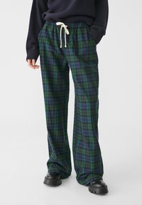 Vihreät ja siniset ruudulliset leveälahkeiset housut, joissa on joustava vyötärö ja nyöri, sekä sileä kangas ja sivutaskut.