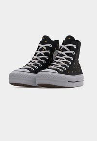 Μαύρα sneakers ψηλά με λευκά κορδόνια και σόλες, διακοσμημένα με μικρά χρυσά αστέρια και ένα κυκλικό λογότυπο στην πλευρά.