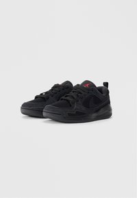 Zapatillas deportivas negras con parte superior de malla, acentos de gamuza y suela de goma. Presentan cordones negros y un logo de la marca en rojo en la lengüeta y en el lateral.