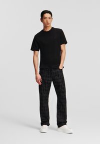Tricou negru din bumbac și pantaloni negri cu un model subtil, asortați cu adidași albi. Un look simplu și contemporan.
