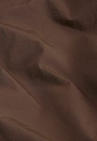 Bruine stof met een gladde, licht gekreukelde textuur, die subtiele glans en natuurlijke kleur- en lichtvariaties toont.