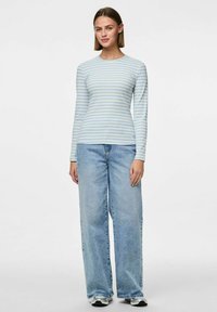 Ljust blå och vit randig långärmad topp med rund halsringning, tillsammans med löst sittande blå jeans och svarta sneakers.