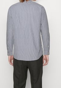 Blauwe en witte gestreepte langomslagen shirt met een knoopkraag, gestructureerde stof en knoopaccenten op de manchetten, gezien van achteren.