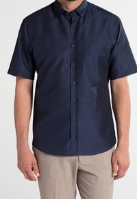 Chemise à manches courtes, de couleur bleu marine foncé, à boutons avec col et une poche poitrine unique, fabriquée à partir d'un tissu texturé.