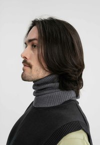 Grijze geribbelde coltrui met een donkere vestoverlay; kortgeknipte zijaanzicht van een persoon met lang, golvend haar.