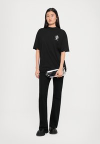T-shirt oversize nera con graphic sul lato sinistro del petto, abbinata a pantaloni neri attillati e una borsa a tracolla in vinile trasparente. Calzature nere chunky.