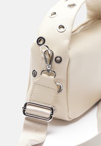Cream faux leather handbag with silver grommets and hardware. Features a detachable strap and a zippered opening for closure.