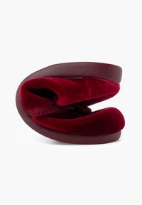 Zapatilla de terciopelo burdeos con una textura suave y diseño curvado, que cuenta con una suela de goma marrón y una forma redondeada para mayor comodidad.