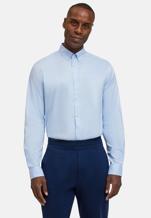 Hellblaue Hemd mit langen Ärmeln und klassischem Kragen, kombiniert mit marineblauen Hosen. Das Hemd verfügt über eine subtile Textur und Knopfdetails.