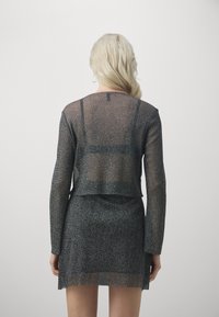 Completo due pezzi nero con texture luccicante, composto da un top corto a maniche lunghe e una mini gonna aderente, con elementi trasparenti e orlo dritto.