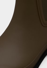 Καφέ λαστιχένια μποτάκια αστραγάλου με λείο φινίρισμα, στρογγυλεμένη μύτη και ελαστική πλευρική επένδυση. Μαύρη σόλα με διακριτική υφή στο κάτω μέρος.