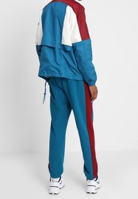 Ensemble de survêtement coloré comprenant une veste bleue avec des accents rouges et blancs et un pantalon bleu assorti, le tout en tissu lisse et léger.