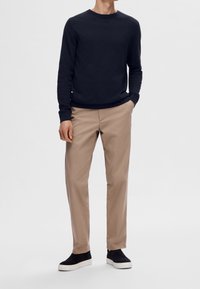 Námořnický svetr s kruhovým výstřihem, béžové chinos kalhoty a černé slip-on tenisky. Svetr má texturovaný povrch; chinos jsou rovného střihu a hladké.