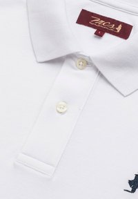 Polo bianco con tessuto testurizzato, caratterizzato da un'etichetta bordeaux, due bottoni e un logo ricamato blu navy sul lato sinistro.