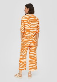 Oranges Zweiteiler-Outfit mit einer lockeren Bluse und weiten Hosen mit weißen Zebrastripes. Hergestellt aus leichtem Stoff, entspannte Passform.