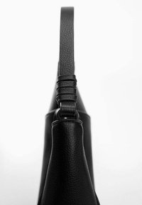 Sac à main en cuir noir montré de côté, avec une finition texturée, une sangle fine et des bords arrondis distinctifs.